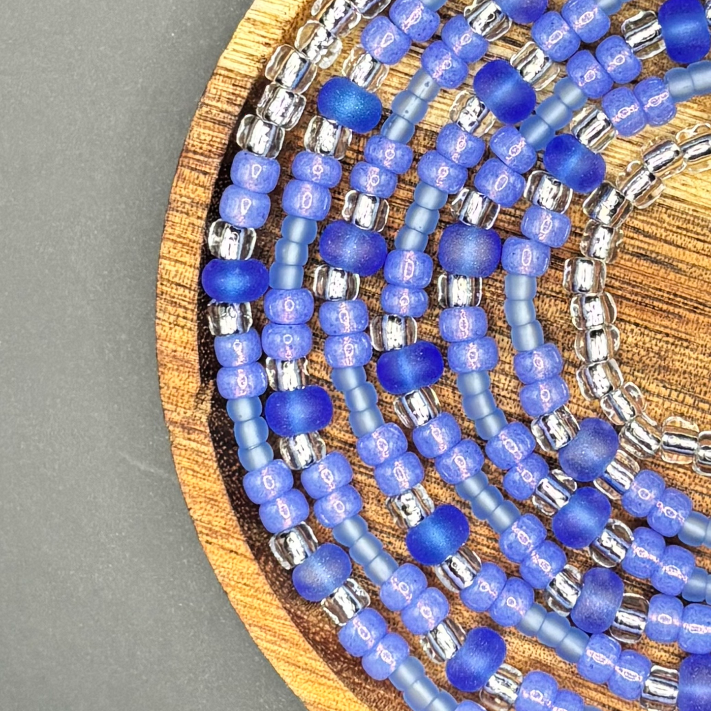 Electric Sky waist bead set featuring rich electric purple and matte lavender seed beads with frosted violet rounds and silver-lined accents, arranged on a wooden display dish against a dark background, created by Waisted by Design. 