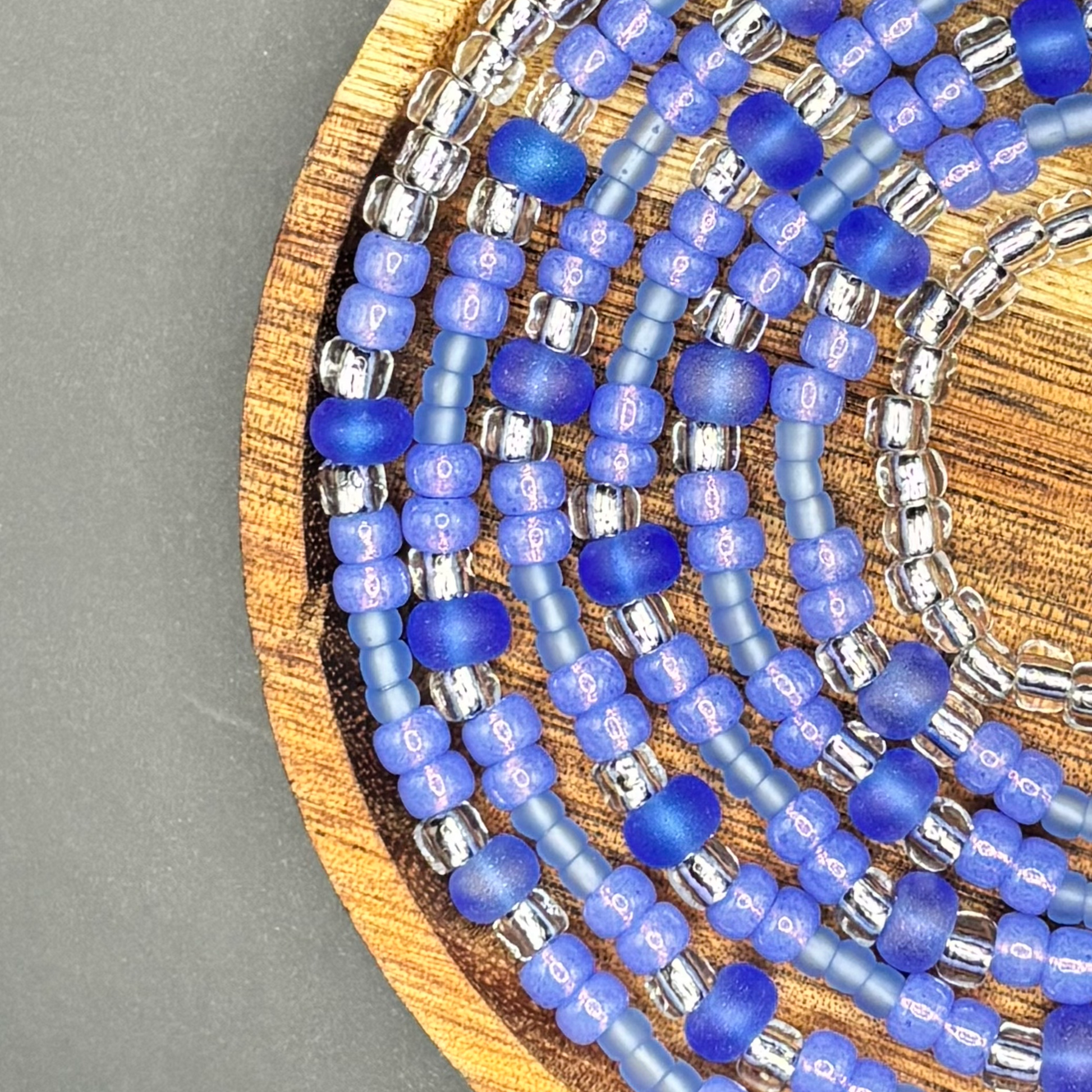 Electric Sky waist bead set featuring rich electric purple and matte lavender seed beads with frosted violet rounds and silver-lined accents, arranged on a wooden display dish against a dark background, created by Waisted by Design. 