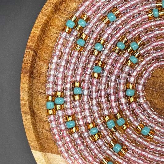 Pink waist beads made with shimmering seed beads in soft blush and rose tones displayed on a wooden stand