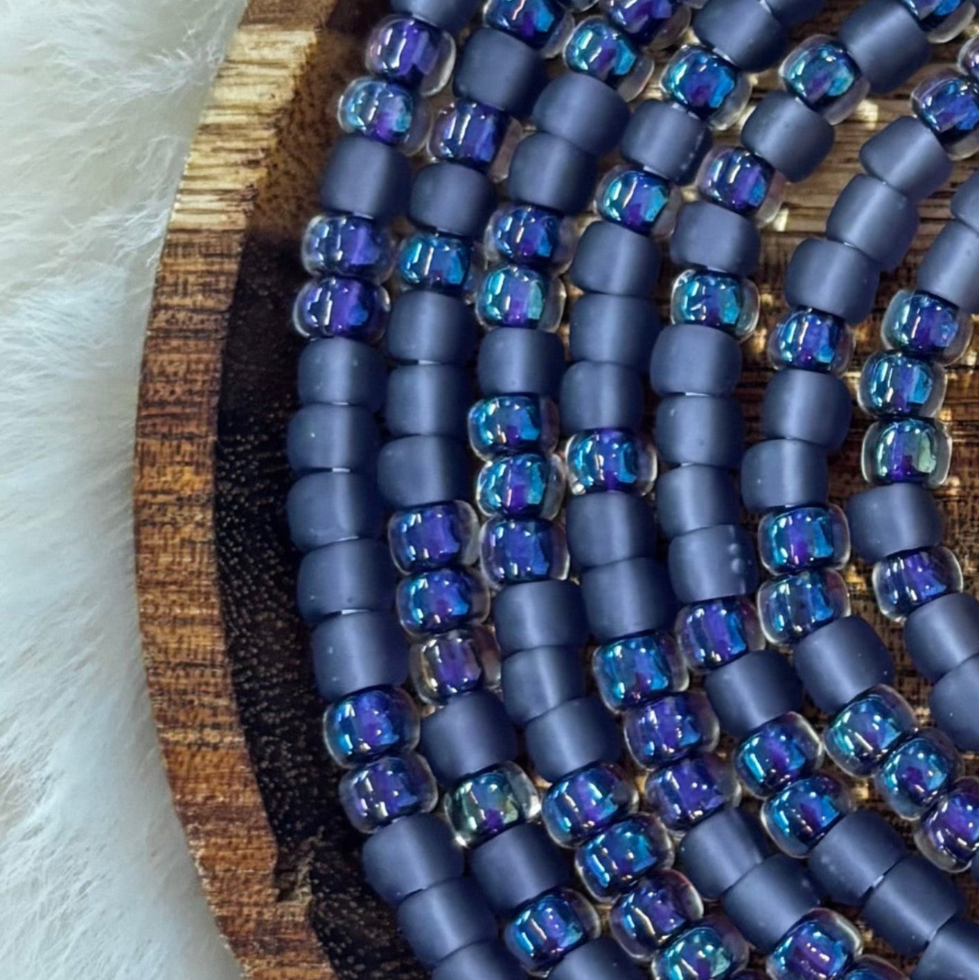 Passion waist beads featuring matte midnight purple seed beads with iridescent violet and blue glass accents on a wooden tray by Waisted by Design.