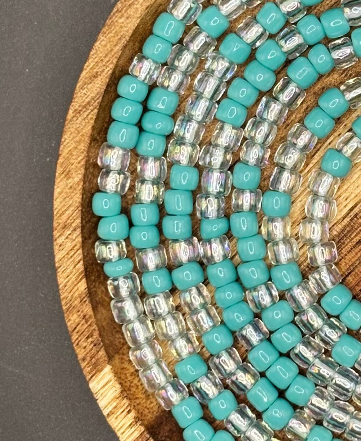 Turquoise and clear iridescent waist beads arranged on a wooden tray, featuring soft aqua seed beads paired with luminous crystal accents from Waisted by Design.